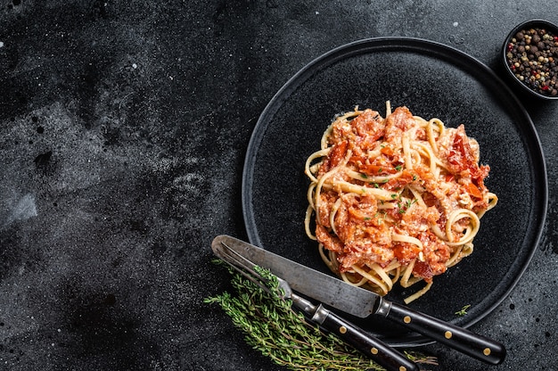 Feta pasta with Oven baked cherry tomatoes on a plate. Black background. Top view. Copy space.