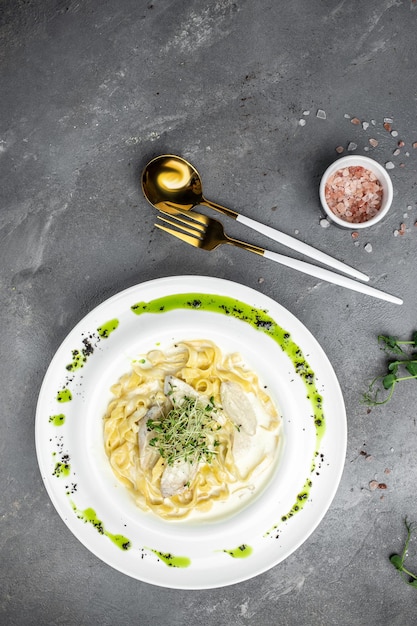 Fettuccine alfredo in a creamy sauce with chicken parmesan on white plate Pasta alfredo with chicken Italian cuisine vertical image top view place for text