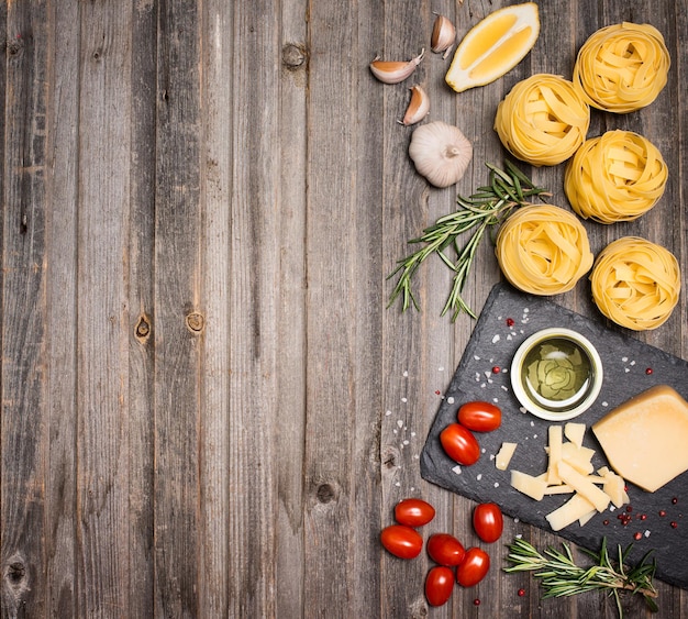 Fettuccine background frame with ingredients for cooking pasta on weathered wood top view