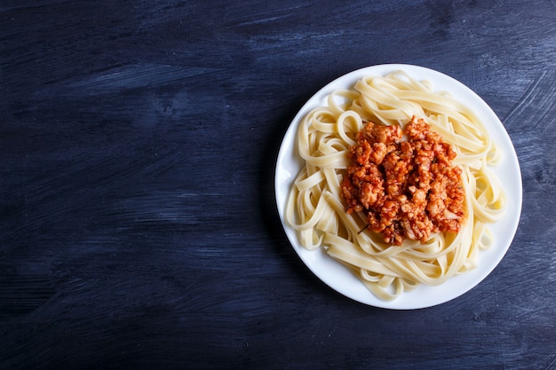 Fettuccine bolognese pasta with minced meat on black wooden background.