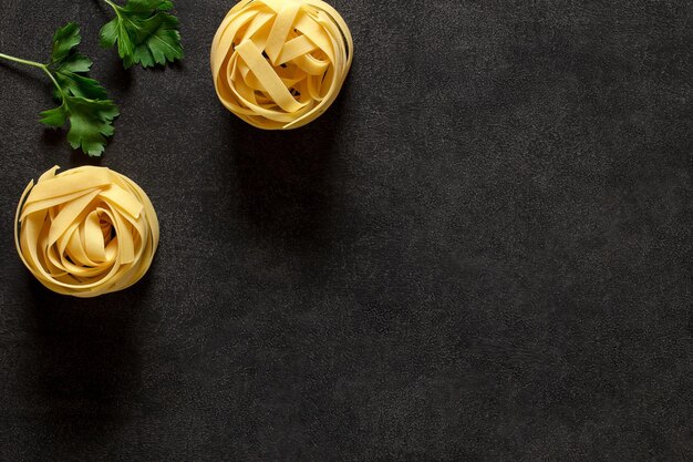 Fettuccine pasta two raw uncooked nest and parsley ingredients for an Italian dish on dark background top view space to copy text