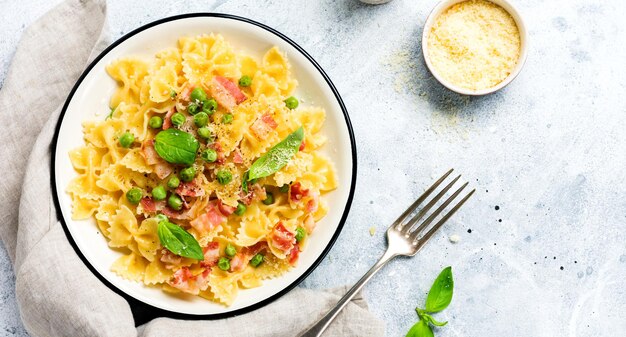 Fettuccine pasta with bacon and green peas and parmesan cheese in light plate on old gray concrete background. Top view.