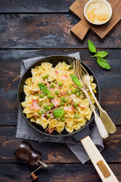 Fettuccine pasta with bacon and green peas and parmesan cheese in old pan on old dark wooden surface