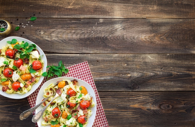 Fettuccine pasta with baked tomatoes bacon and mozzarella cheese on rustic wooden background