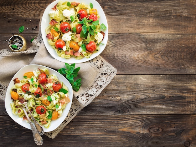 Fettuccine pasta with baked tomatoes bacon and mozzarella cheese on rustic wooden background