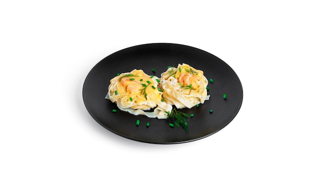 Fettuccine pasta with shrimp in cream sauce on black plate isolated on white. Nests of pasta with seafood and cheese.