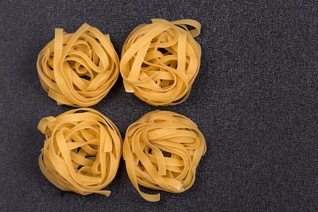 Fettuccine or Tagliatelle on gray background. Spaghetti nests. Italian cuisine. Dry uncooked pasta