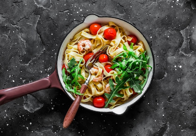 Fettuccine with shrimp cherry tomatoes and arugula in a frying pan on a dark background top view