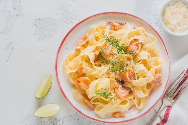 Fettucine pasta with salmon and parmesan cheese in creamy sauce in ceramic plate on old light concrete surface