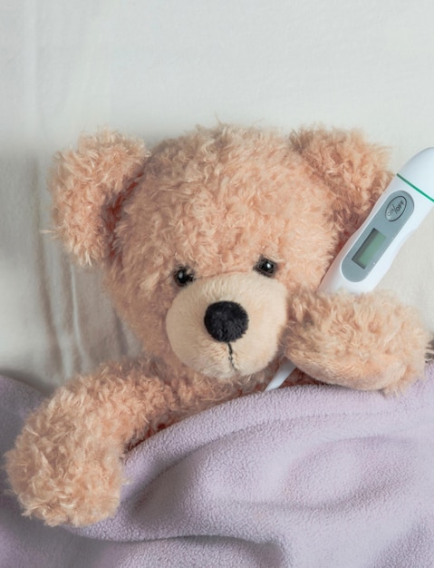 Fever cold flu Cute teddy with a thermometer in bed covered with a warm blanket