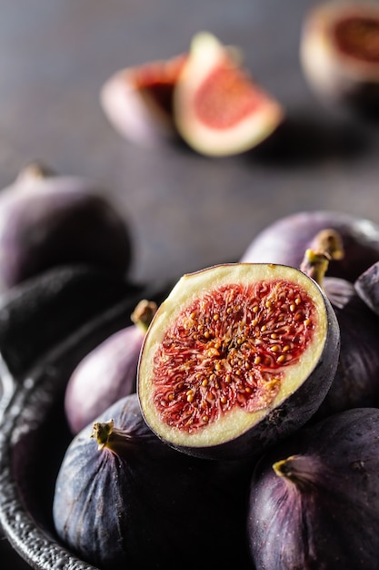 A few figs in a black bowl on an dark concrete table.