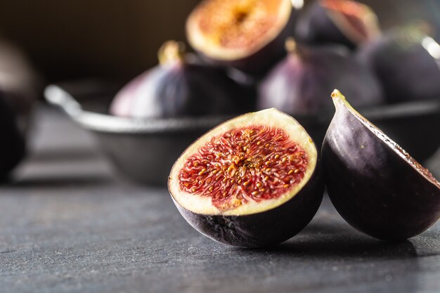 A few figs in a black bowl on an dark concrete table.