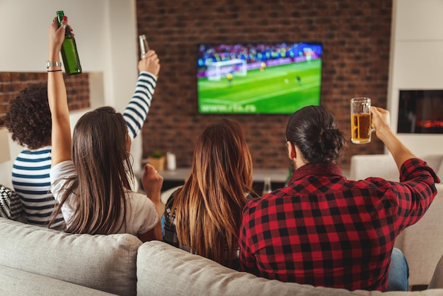 A few friends, fans of sports, love spending their free time at home together looking football game at TV. They are screaming and gesturing for a victory.