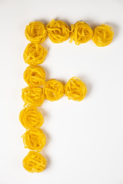 Few homemade fettuccine nest in the shape of the letter F isolated on white background