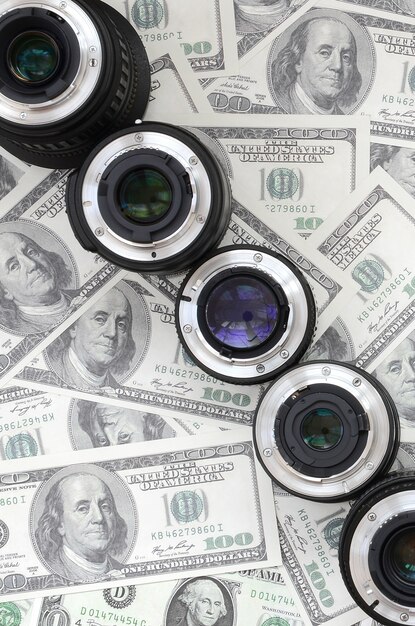 A few photographic lenses lies on the background of a lot of dollar bills. 