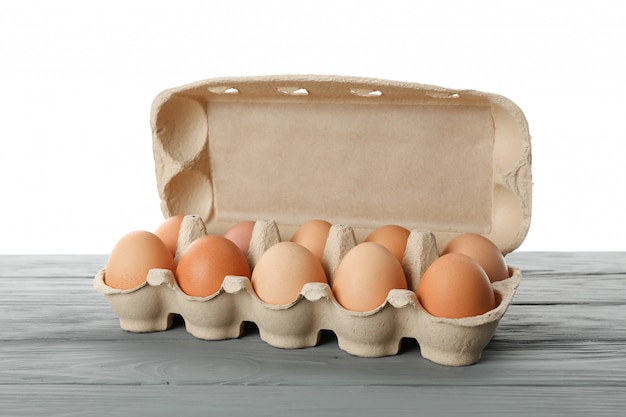Foto poche uova crude del pollo in contenitore di cartone sulla tavola di legno contro bianco