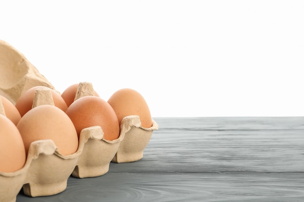 Photo few raw chicken eggs in carton box on wooden table against white