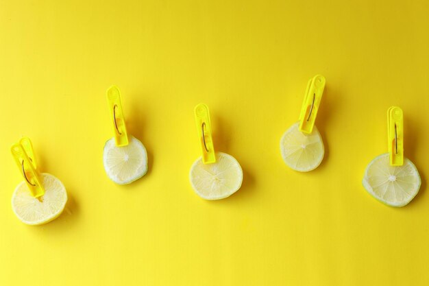 Few rounded lemon slices held with clothes pegs or clothes pins on yellow background Cute wallpaper