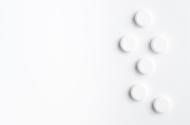 A few white capsule pills on white background closeup