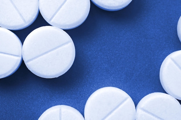 A few white tablets lie on a bright phantom classic blue color background surface Background image on medical and pharmaceutical topics