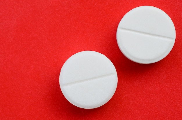 A few white tablets lie on a bright red background surface