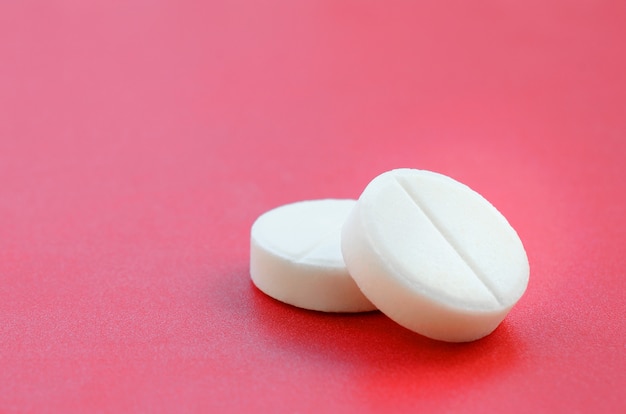 A few white tablets lie on a bright red background surface. 