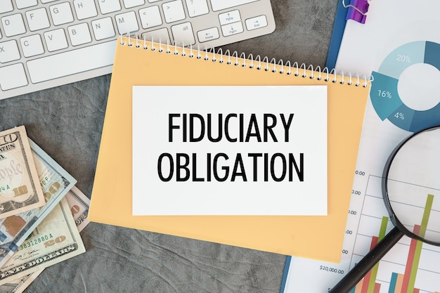 Fiduciary Obligation is written in a document on the office desk with office accessories, money, diagram and keyboard