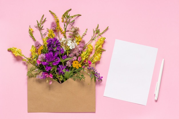 Field flowers in craft envelope and white empty paper card