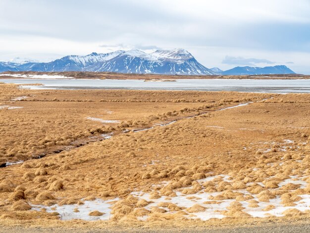 Field with snow in winter with moutains in background under cloudy blue sky in Iceland