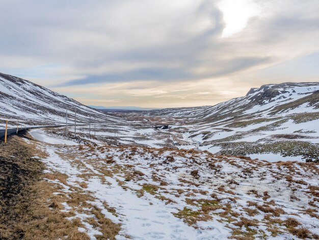 Field with snow in winter with moutains in background under cloudy blue sky in Iceland