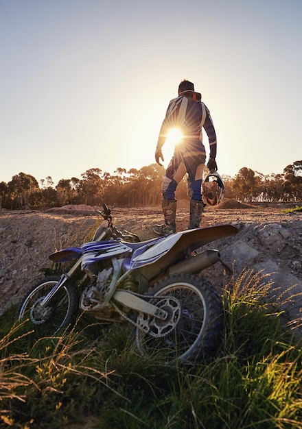 Foto fiets off-road sport en man met helm op het spoor bij zonsondergang voor wedstrijd race of training challenge fitness en motorfiets met persoon in sportkleding uitrusting buiten voor actie of kracht van achteren