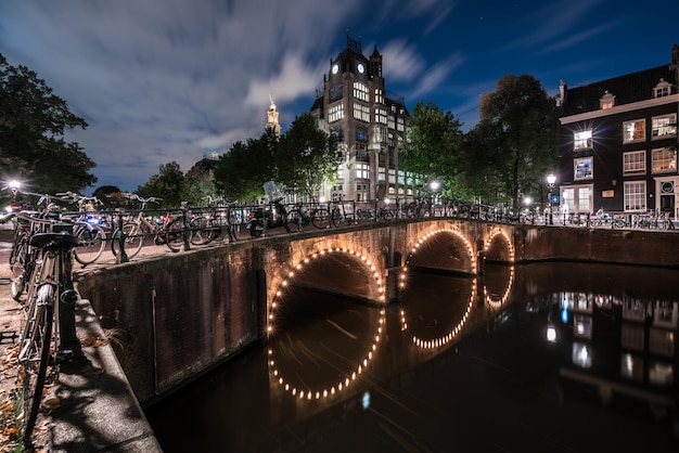 Fietsen geparkeerd op verlichte boogbrug over kanaal tegen bewolkte hemel in de schemering
