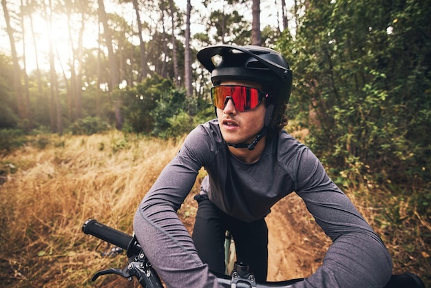 Fietser fiets en bos op avontuur in de natuur voor gezondheid, fitness en wellness Man fiets en zonnebril in het bos voor reizen met helm op trainingsoefening of training op pad door bomen