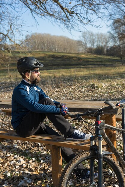 Fietser in broek en fleecejack op een moderne carbon hardtail-fiets met een luchtgeveerde vork rijdt offroad De man rust op een bankje in het herfstpark