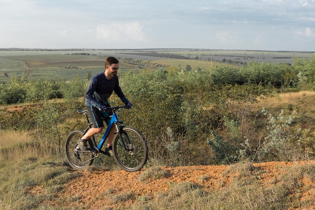 Fietser in broek en fleecejack op een moderne carbon hardtail-fiets met een luchtgeveerde vork rijdt offroad De man rust op een bankje in het herfstpark