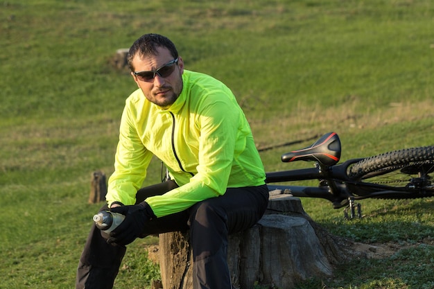 Fietser in broek en groen jasje op een moderne carbon hardtail-fiets met een luchtgeveerde vork De man op de top van de heuvel rijdt op een fiets