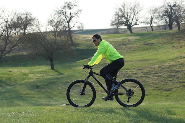 Fietser in broek en groen jasje op een moderne carbon hardtail-fiets met een luchtgeveerde vork De man op de top van de heuvel rijdt op een fiets