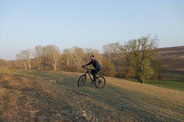 Fietser in korte broek en jersey op een moderne carbon hardtail-fiets met een luchtgeveerde vork die op een klif staat tegen de achtergrond van een fris groen lentebos