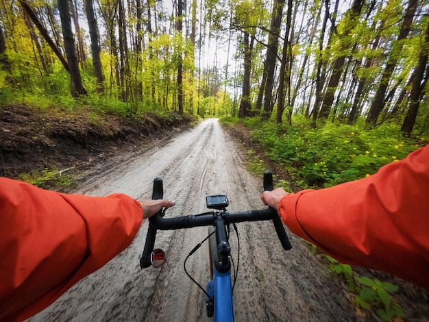 Foto fietser op een grindfiets die langs een bosweg met groene bomen rijdt