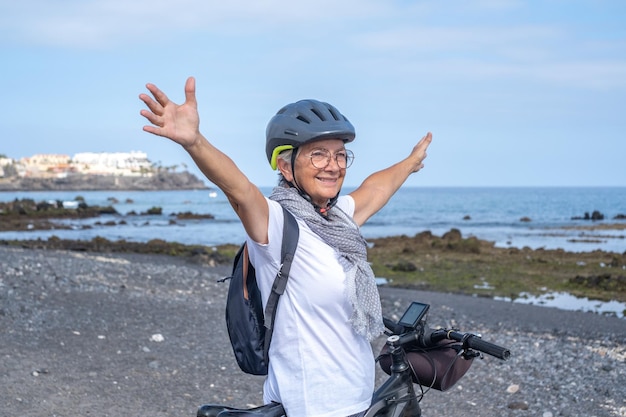 Fietser senior vrouw met helm en rugzak die met haar fiets langs het zeestrand staat