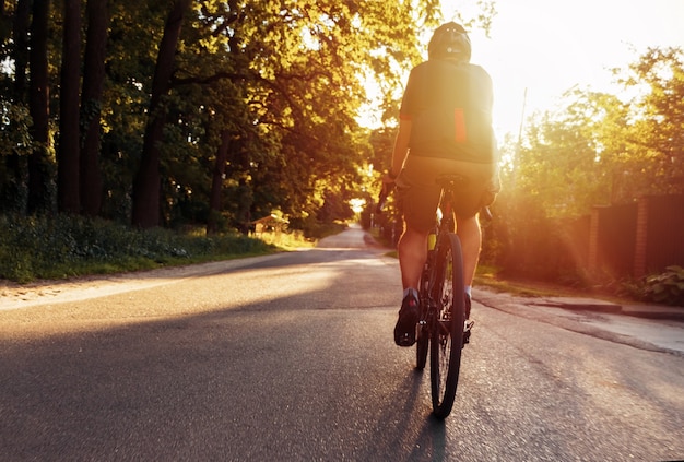 Fietser traint buiten op een fiets op een zomeravond bij zonsondergang.