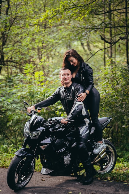 fietsers in leren kleding, man en vrouw, zittend op een zwarte sportmotorfiets in het bos