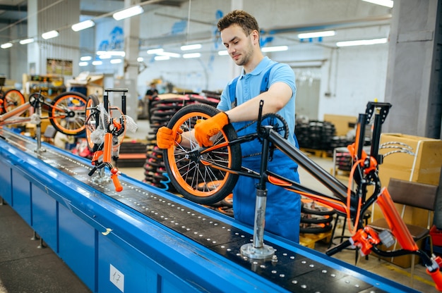 Fietsfabriek, arbeider aan de lopende band, wielinstallatie. mannelijke monteur in uniform installeert fietsonderdelen in de werkplaats