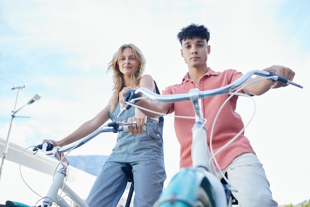 Fietspaar en koolstofvoetafdruk met een man en vrouw die buiten fietsen op een blauwe hemelachtergrond van onderen Portret reizen en pendelen met een jonge man en vrouw fietsen op vakantie