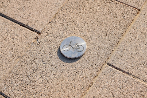 Fietswegmarkering in het park, fietspictogramsymbool op een metalen dop op de stoepstraat in de stad