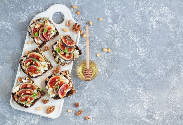 Fig bruschettas with ricotta, nuts and honey on stone table.