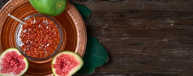 Fig jam in a glass jar on a copper Turkish dish, with halves of fresh figs and a fig leaf next to it