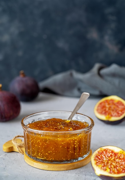 Fig jam in a glass jar with fresh fruits on grey concrete background Vertical banner