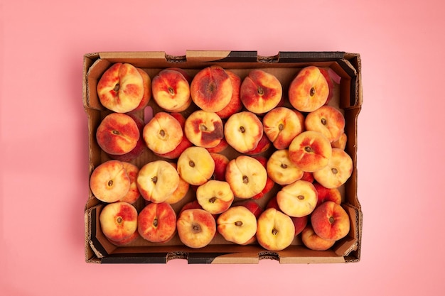 분홍색 배경 위에 있는 종이 상자에 있는 무화과 복숭아 자르기 복숭아 시즌 과일