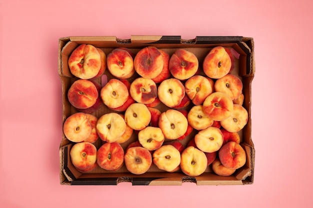 Fig peaches in paper box on pink background top view Crop peaches Season fruits